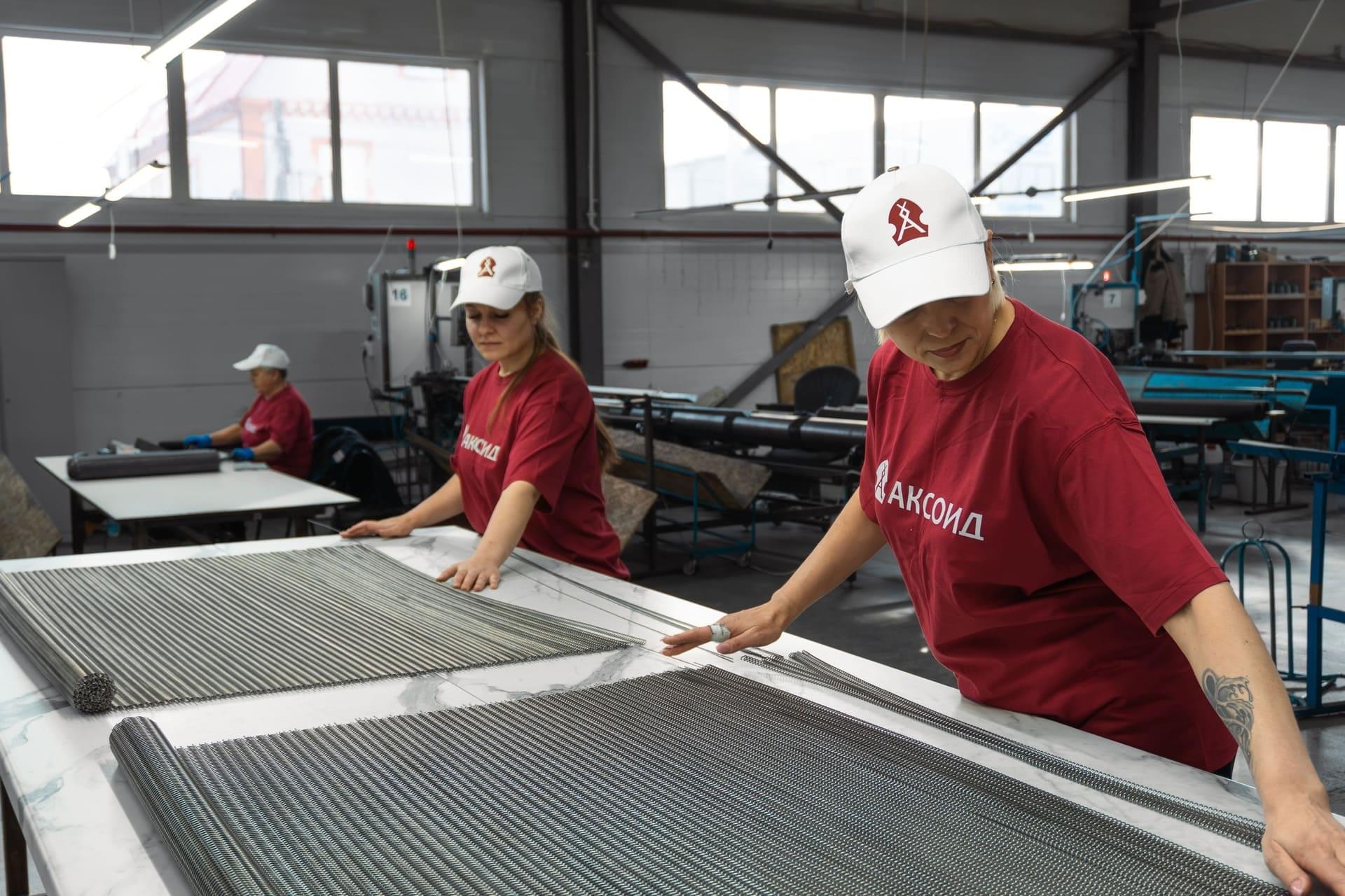 Два работника АКСОИД вставляют металлические прутки в металлическую сетку. Сборка продукции